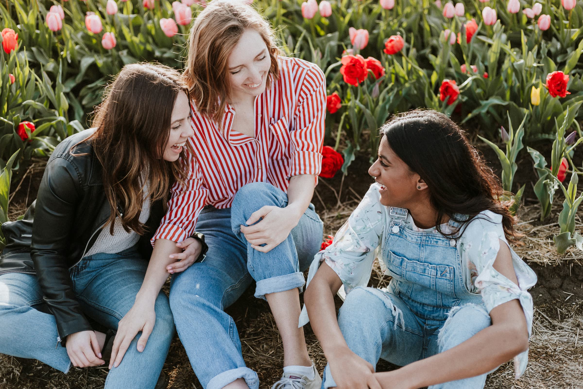 Three friends sitting and laughing among tulips